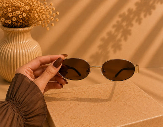 Gold-tone oval sunglasses held in the hand, by LUSHÉ